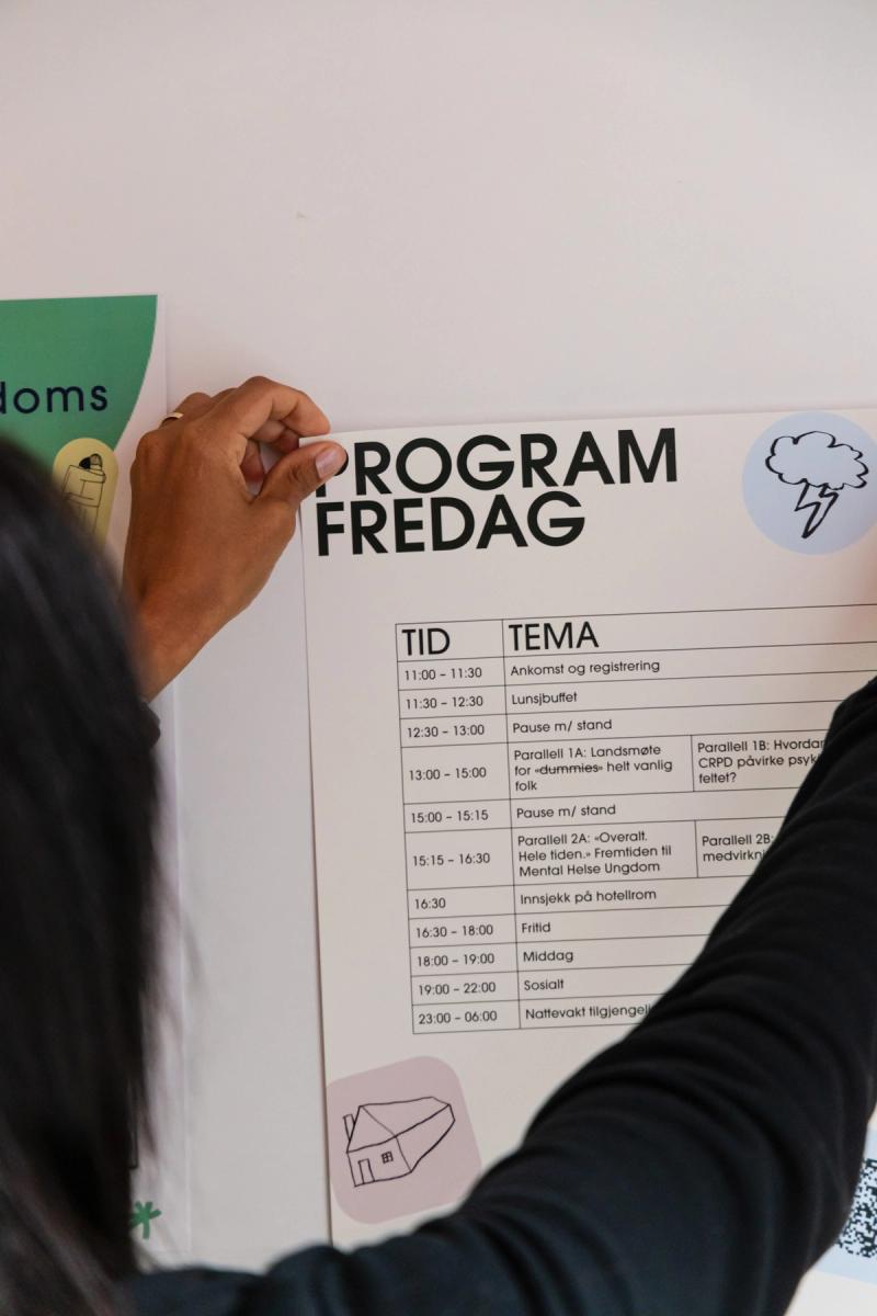 Person som henger opp et program på en vegg.