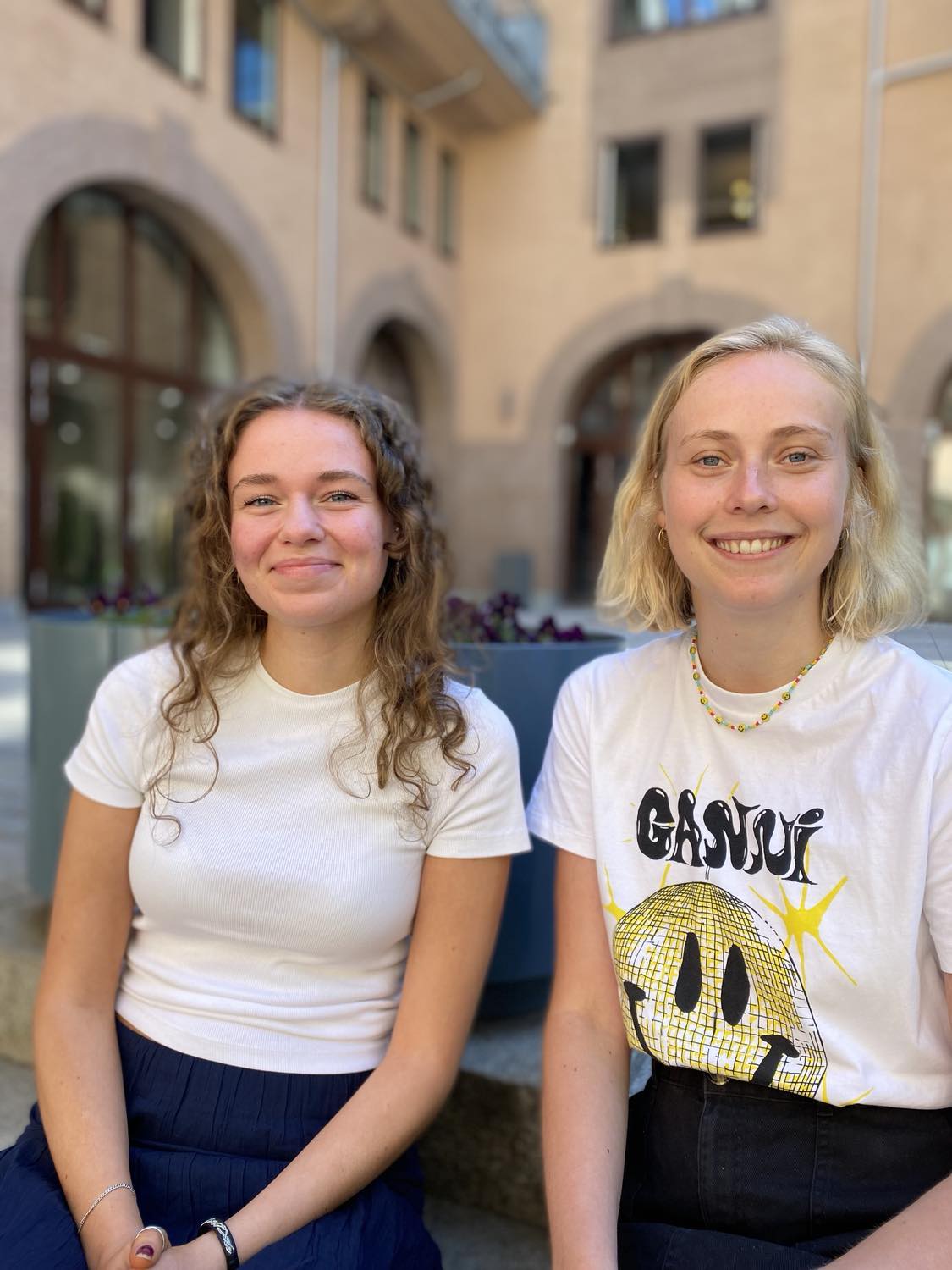 Praksisstudentene Julia og Pernille sitter ute og smiler.