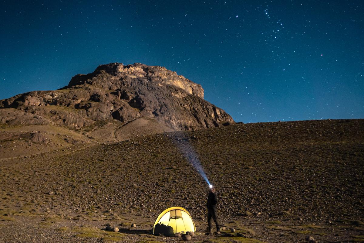 Landskapsbilde på kveldstid, med opplyst telt under stjernehimmel