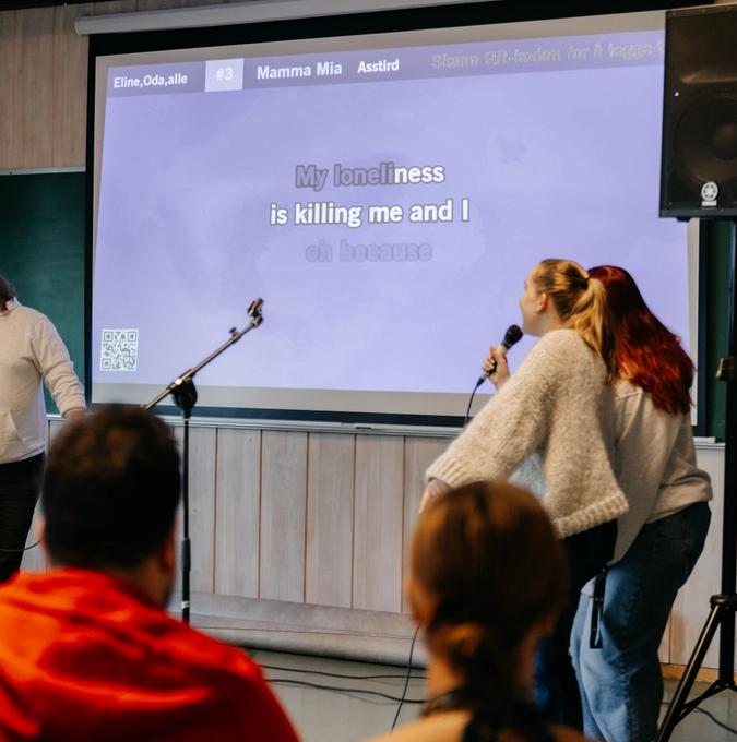 Karaokeskjerm og to som synger i en mikrofon