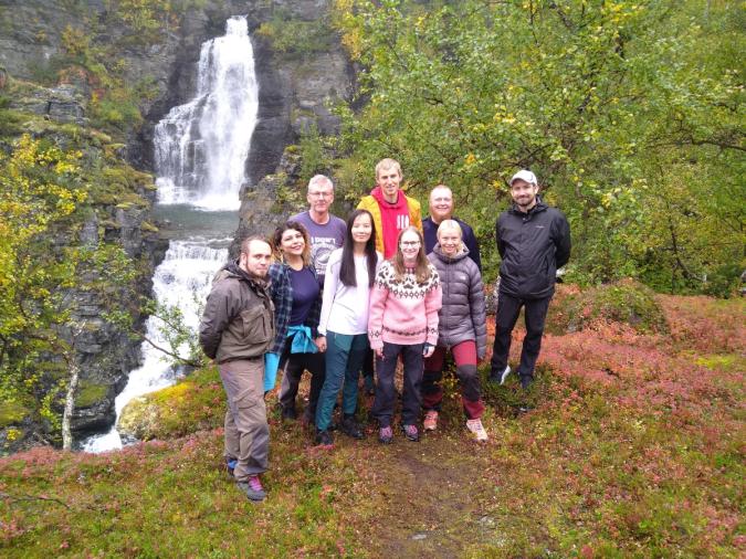Bilde fra en av turene, deltakerne smiler foran en foss