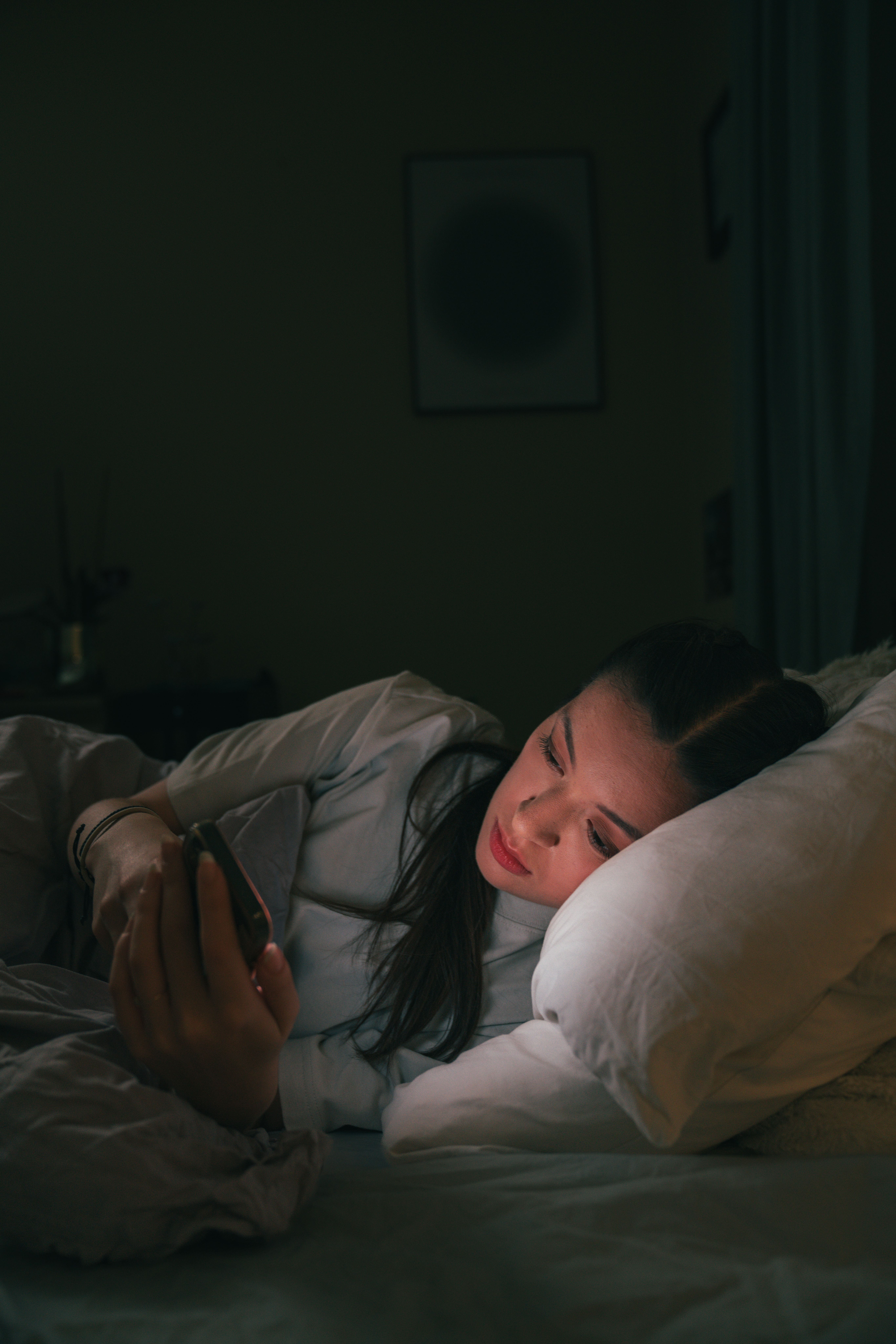 Jente som ligger i senga og ser på mobilen