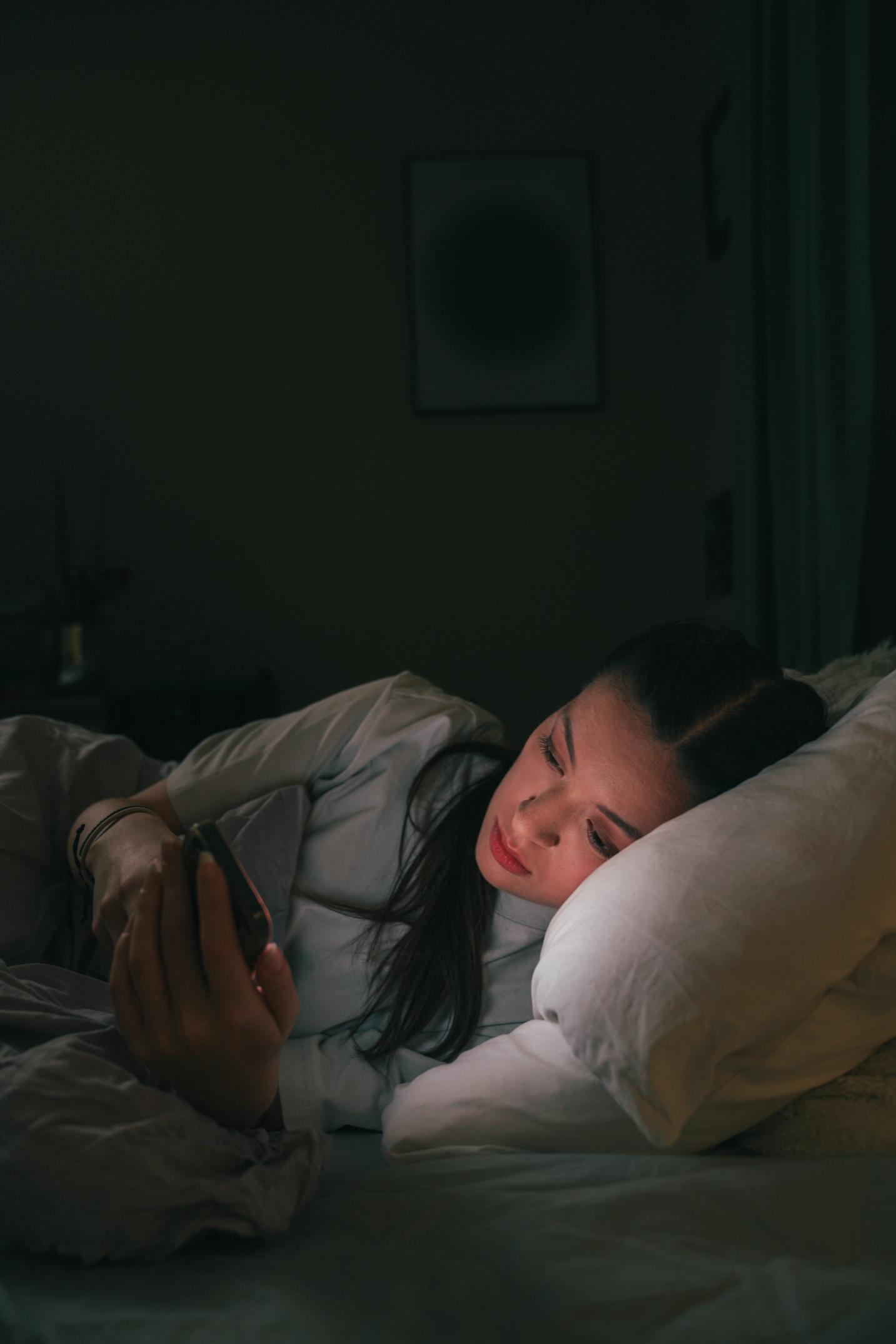 Jente som ligger i senga og ser på mobilen