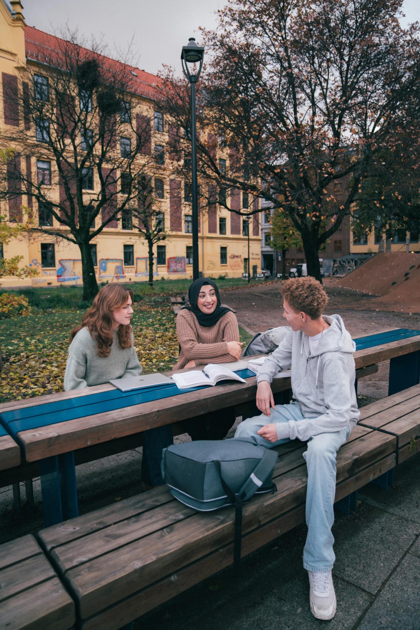 Tre ungdommer sitter i skolegården og gjør lekser