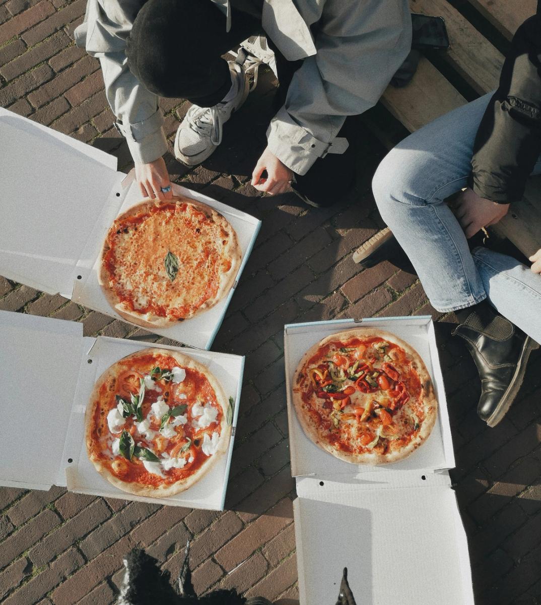 Bilde av en gjeng mennesker rundt noen åpne pizzaesker.