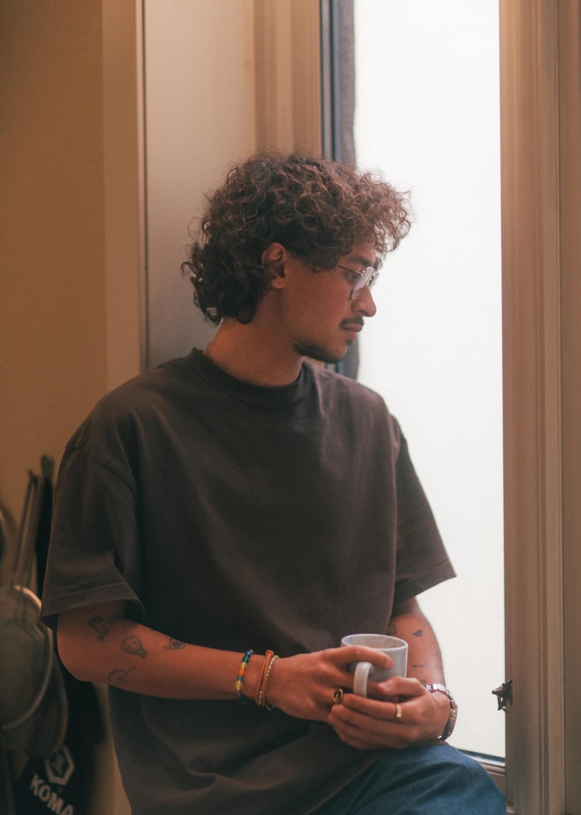 Mann ser ut av vinduet mens han holder en kopp