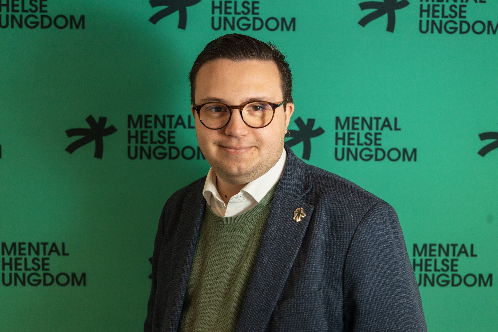 Formelt bilde av Vebjørn foran en vegg med Mental Helse Ungdoms logo på