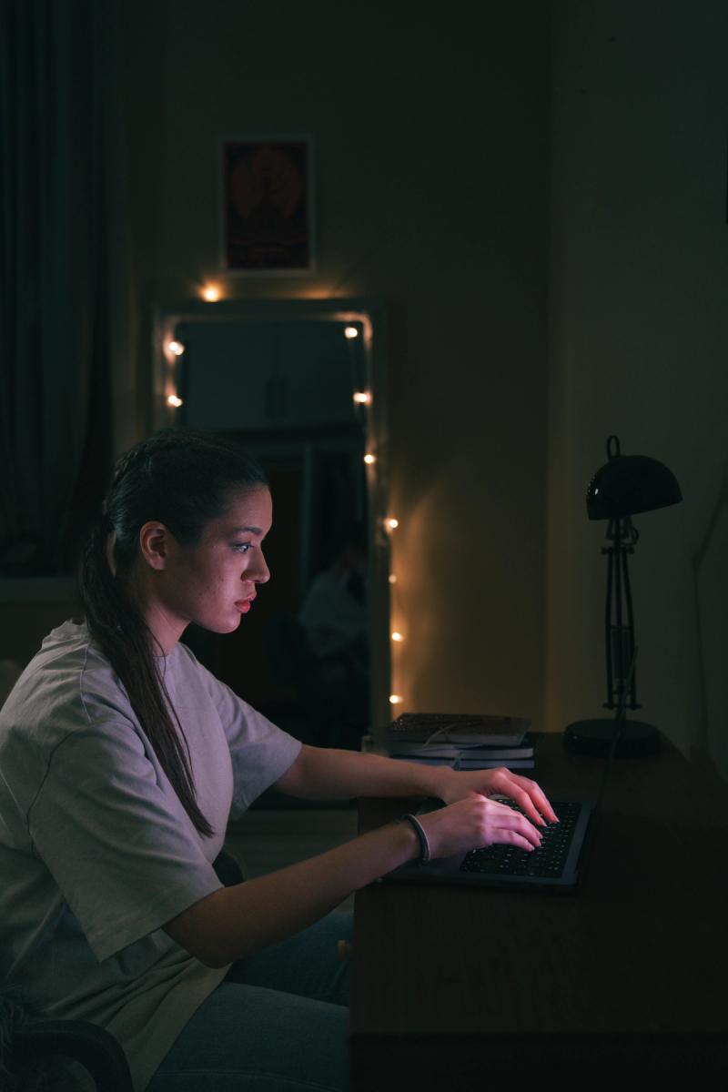 Jente sitter på laptopen ved pulten i mørket