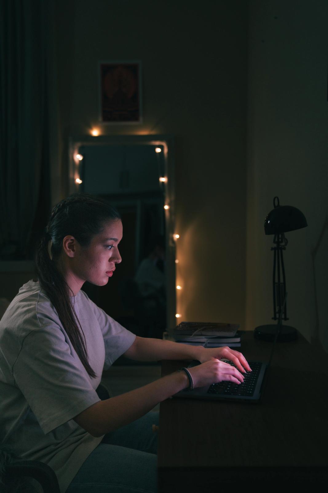 Jente sitter på laptopen ved pulten i mørket