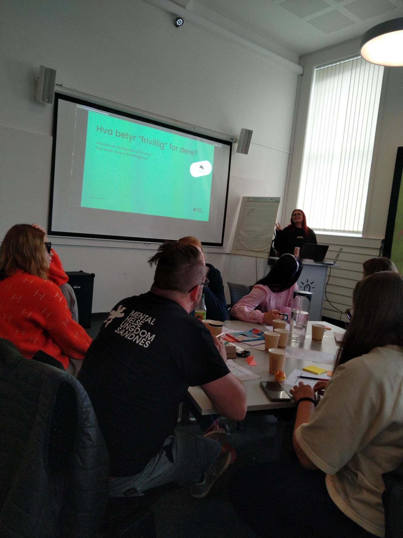 Personer sitter rundt et bord og ser på en presentasjon