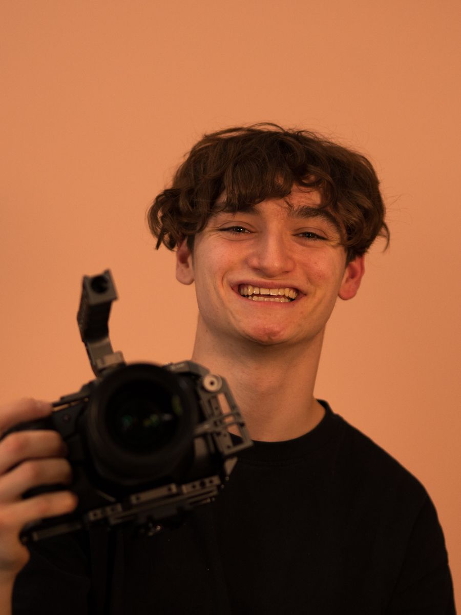 Uformelt bilde av Lukas hvor han smiler og holder opp et kamera