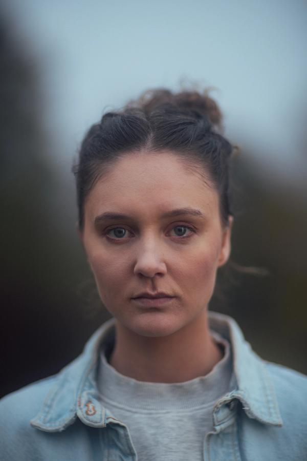 Jente som står utendørs og ser rett inn i kamera. Portrett.