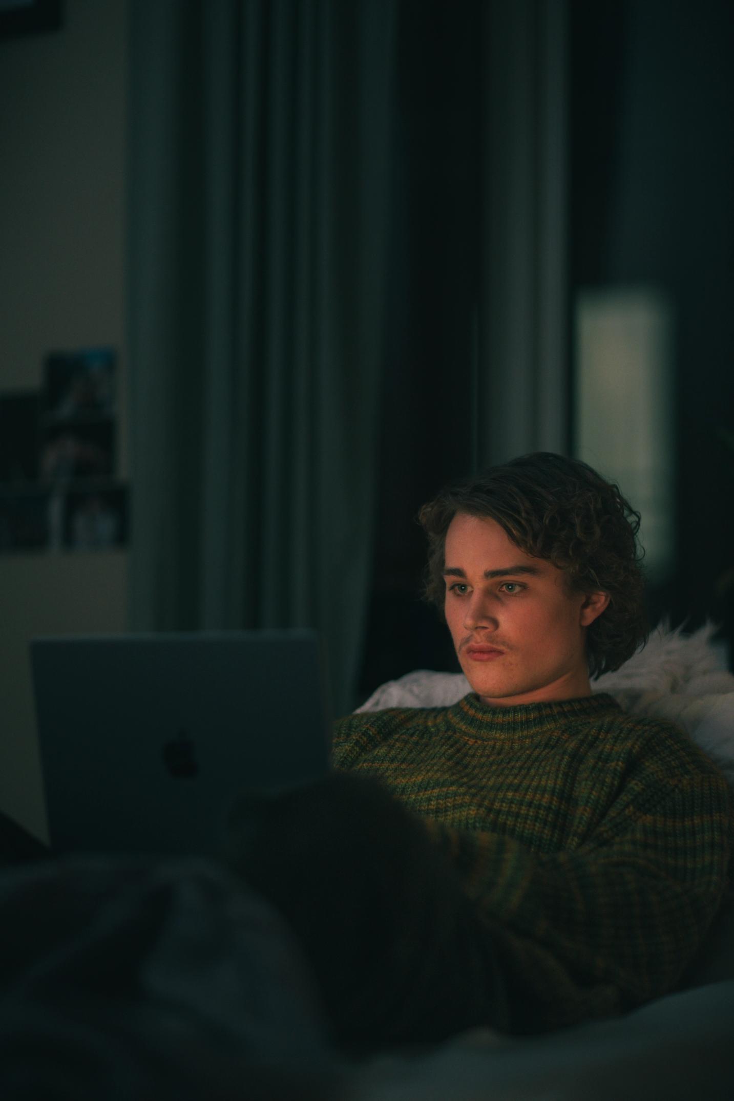 Gutt ser på laptop i mørket i sengen