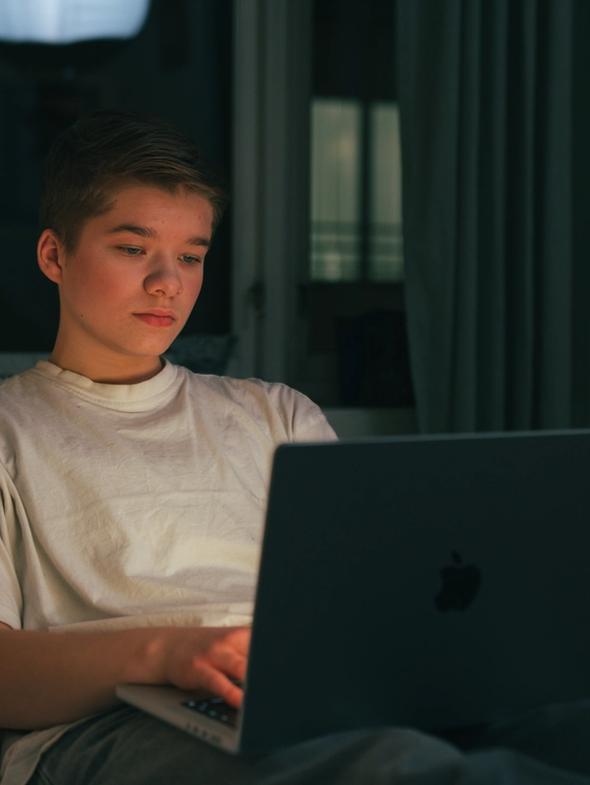 Gutt sitter på laptopen i senga i mørket