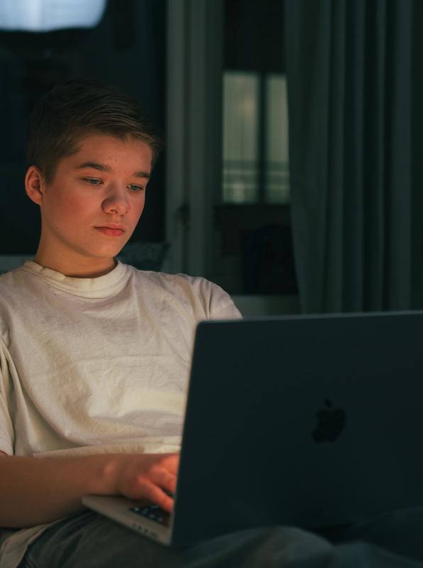 Gutt sitter på laptopen i senga i mørket