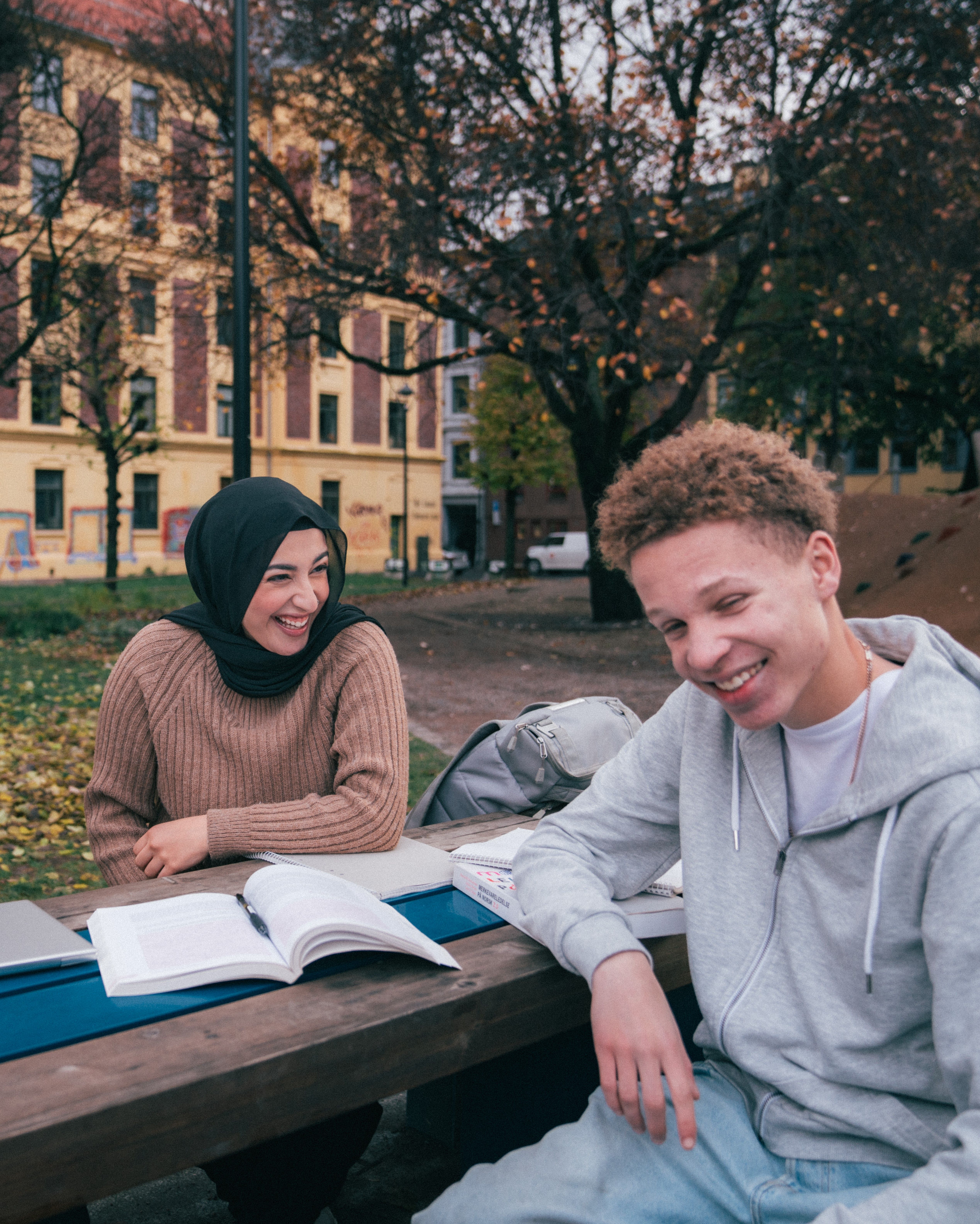 gutt og jente som gjør skolearbeid på en benk og smiler