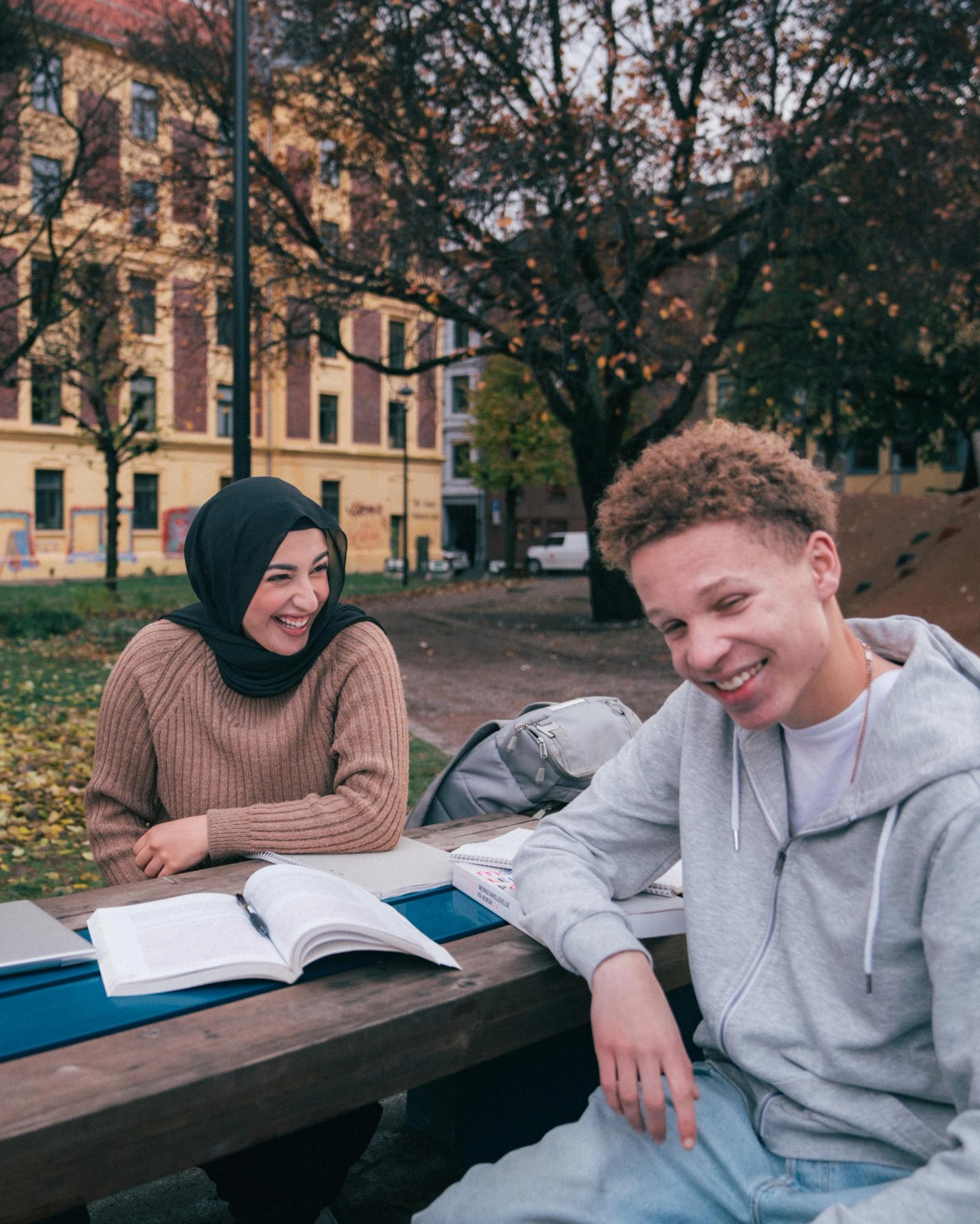 gutt og jente som gjør skolearbeid på en benk og smiler