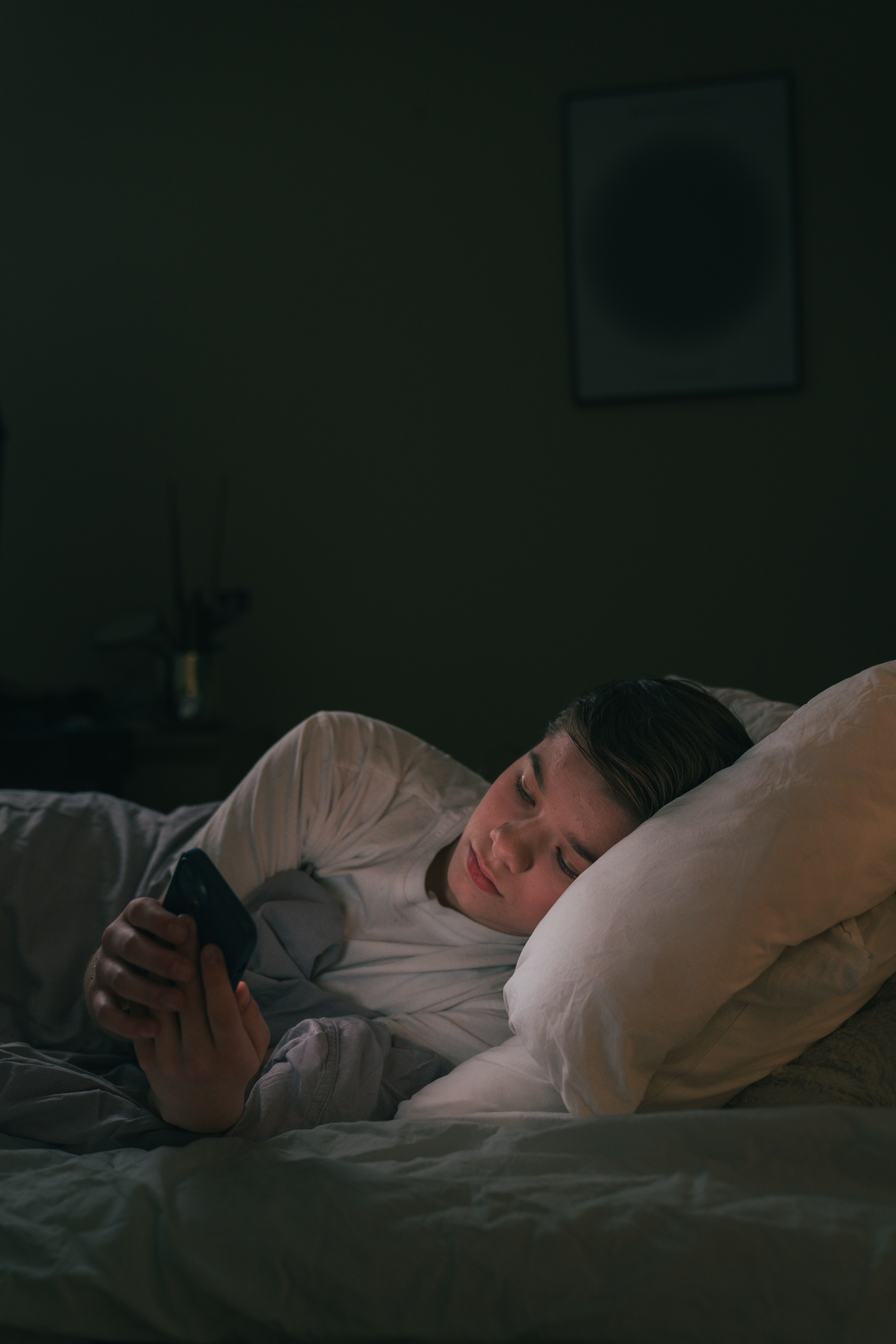 En gutt som er på mobilen i senga.