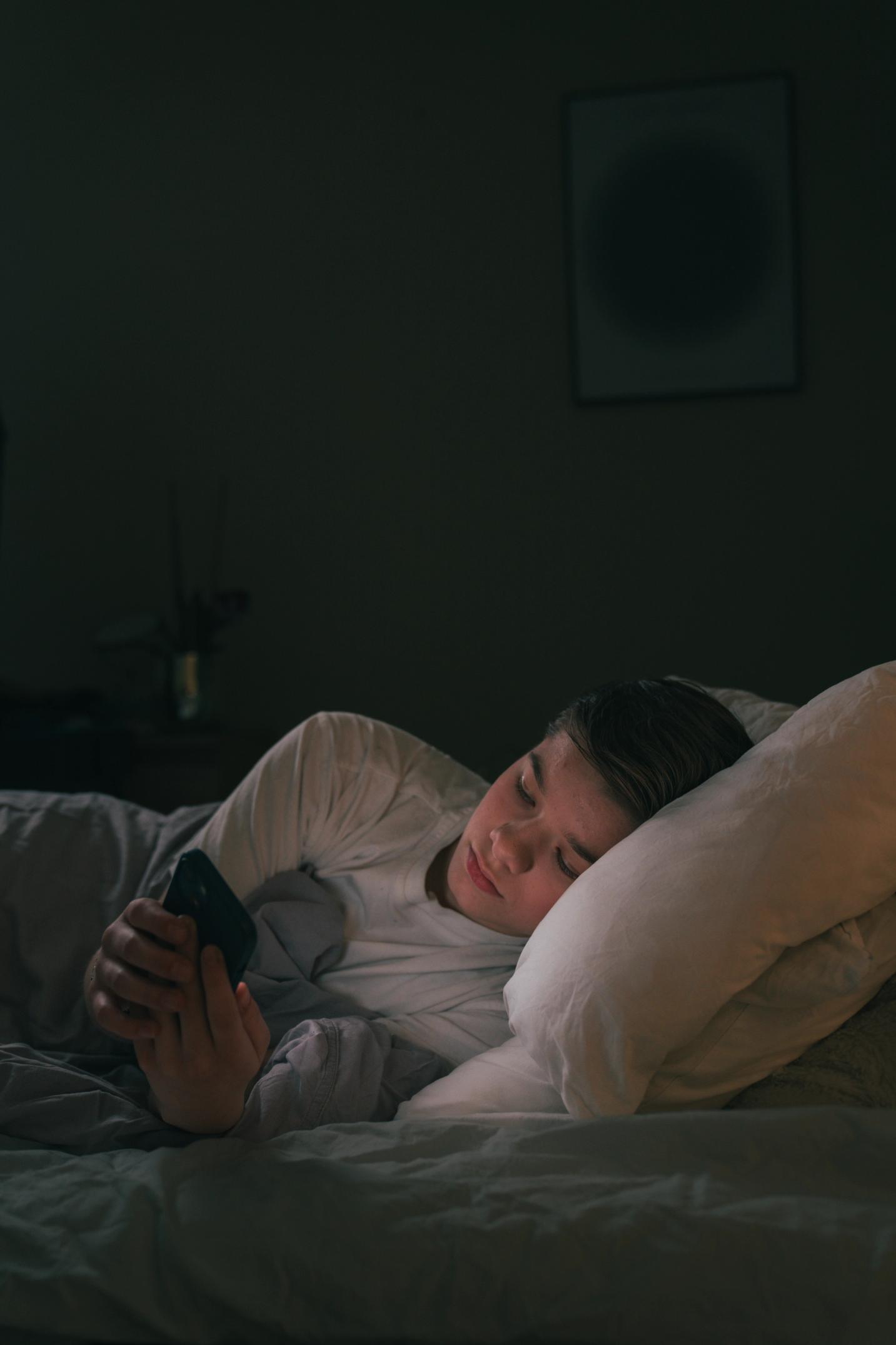 En gutt som er på mobilen i senga.