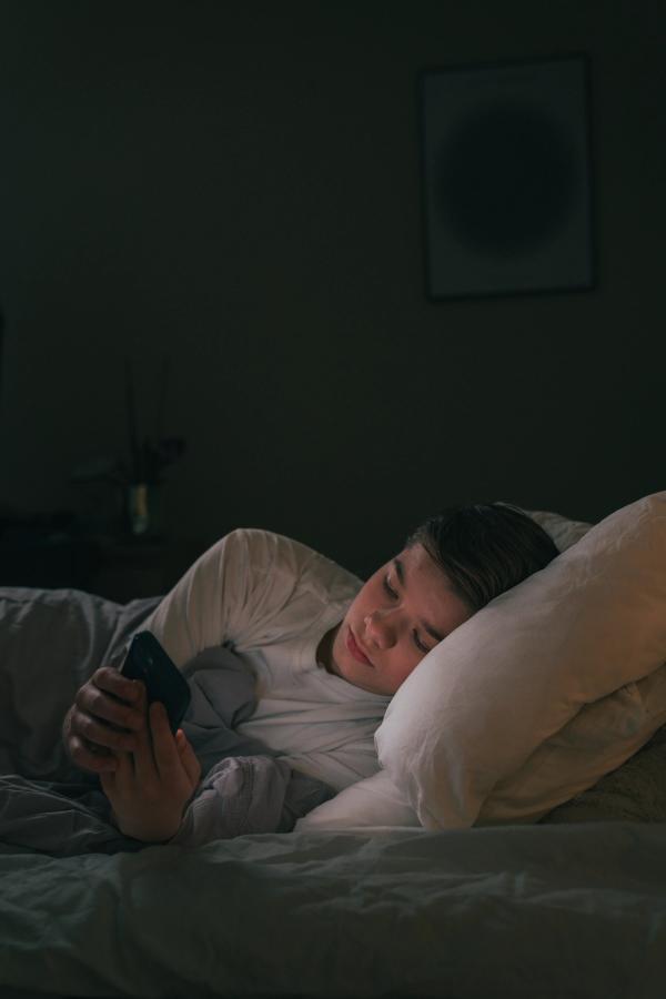 En gutt som er på mobilen i senga.