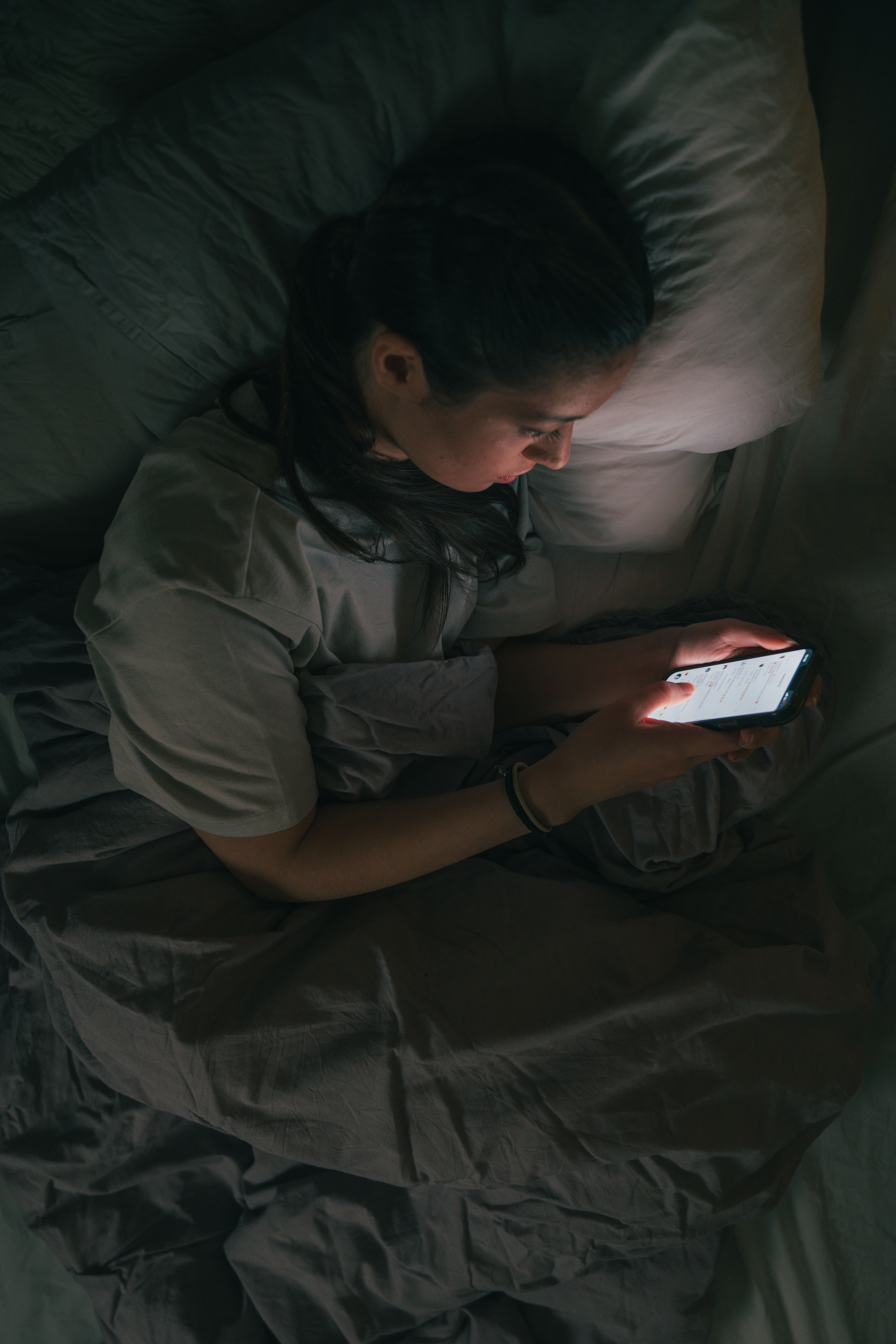 Jente som ligger i senga og ser på mobilen