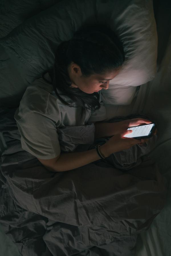 Jente som ligger i senga og ser på mobilen