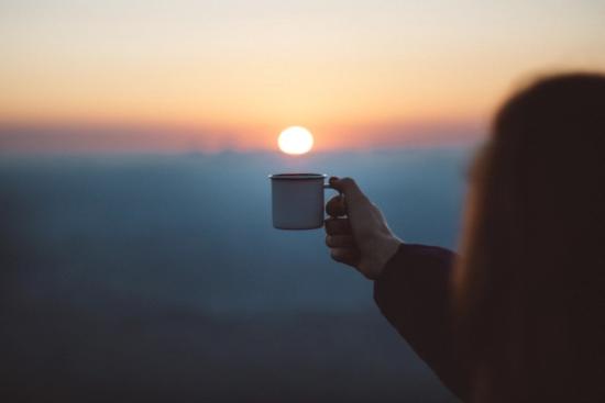 Holding up a cup of coffee to the sunset