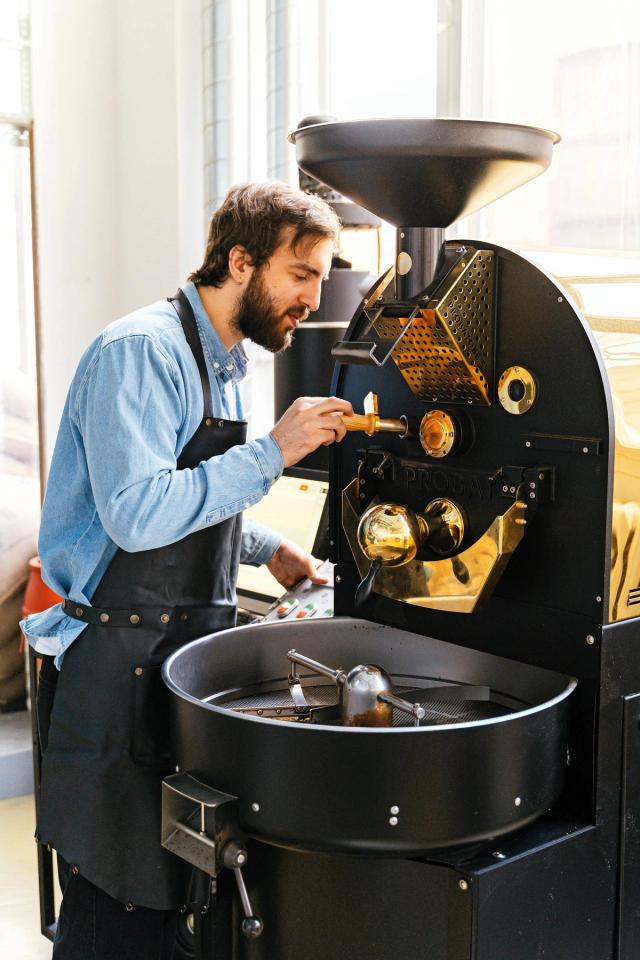 A coffee roaster checks the beans during roasting