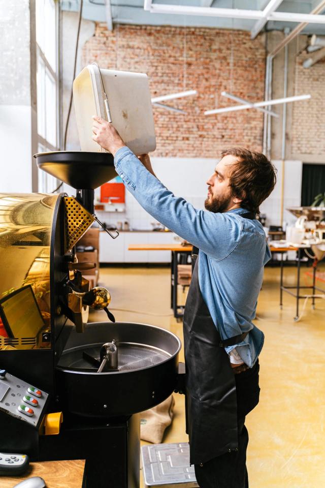 A coffee roaster loads green beans into the roaster's hopper