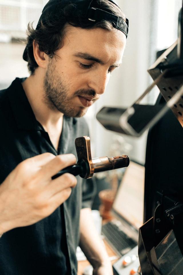 A coffee roaster is checking on the beans he is roasting