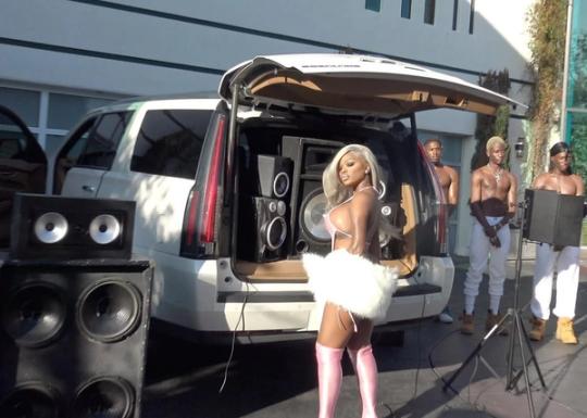 a woman in a bikini is standing in front of a white suv with speakers in the back .