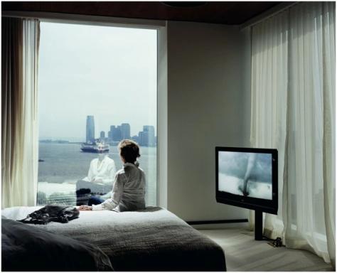 a woman is sitting on a bed looking out a window at a city .