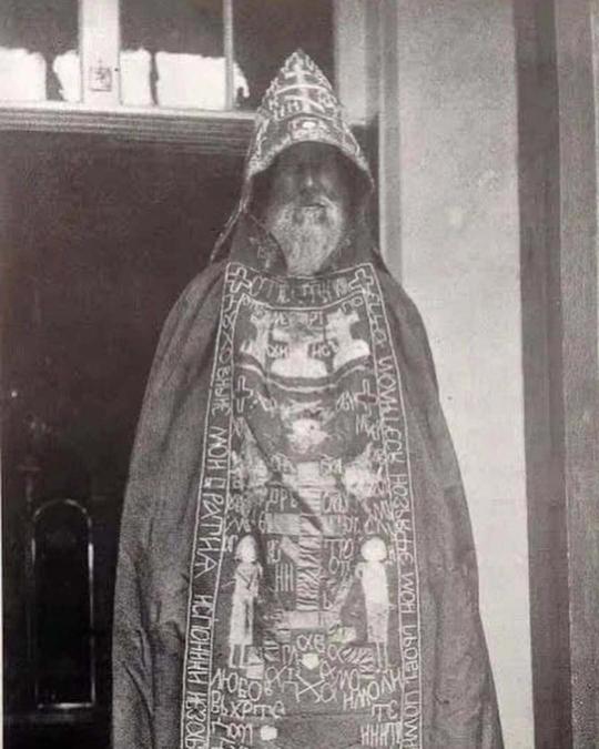 a black and white photo of a man with a beard wearing a cape and a hat .