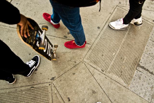 a group of people are standing on a sidewalk holding skateboards .