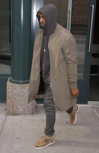 a man wearing a hoodie and a long coat walks down the street