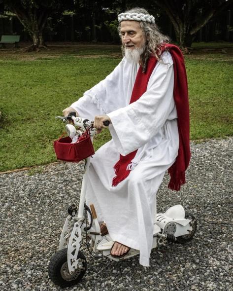 a man dressed as jesus is riding a white scooter