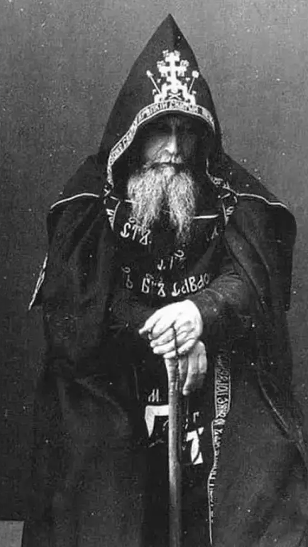 a black and white photo of a man with a beard wearing a hooded cape