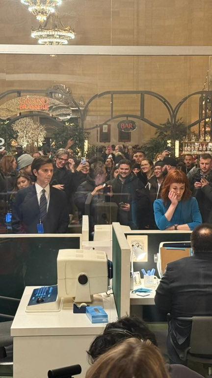 a group of people are standing around a glass office cubicle .