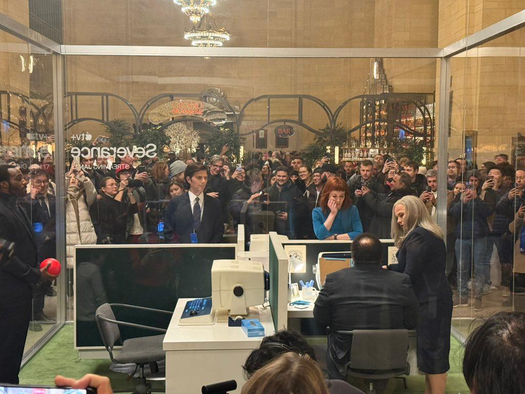 a group of people are standing around a glass office cubicle .