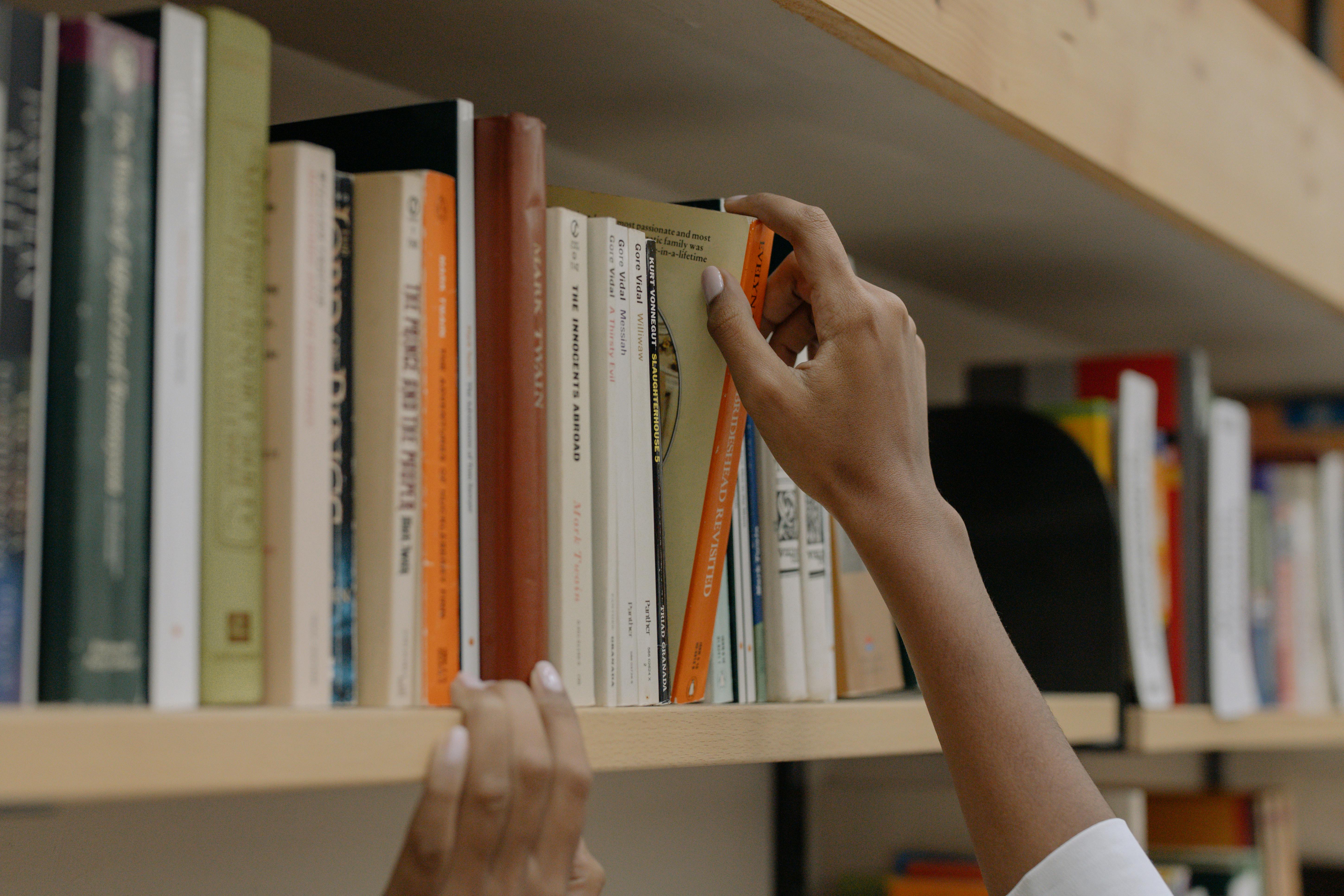 Person Holding A Book On Wooden Shelf