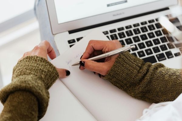 student writing on notebook and using laptop for a research mentorship program