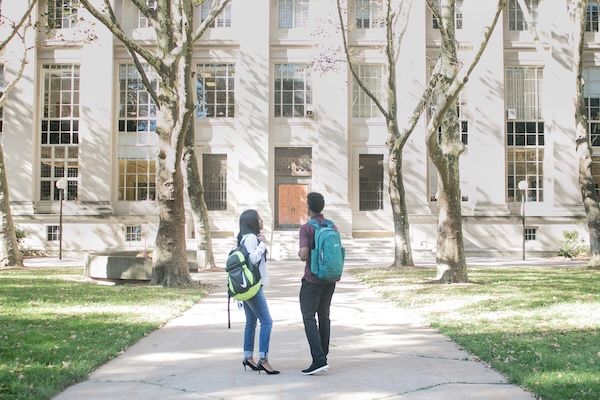 Image shows two college age students standing in front of an unidentified college building. 