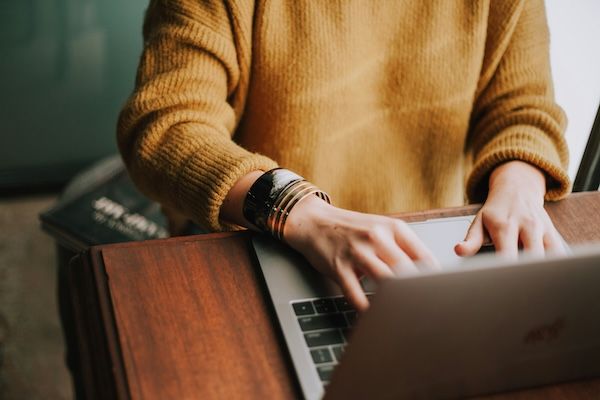 Image shows a woman's arms in a yellow sweater typing on a laptop. 