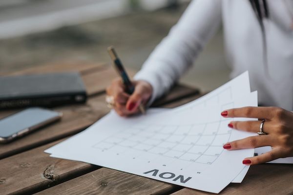 Image is of a women's hands writing on a calendar. Text answers the question "When to send a letter of continued interest". 