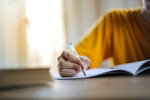 Photo depicts hand writing in a notebook with a pen. Content answers the question "What to include in a letter of continued interest". 