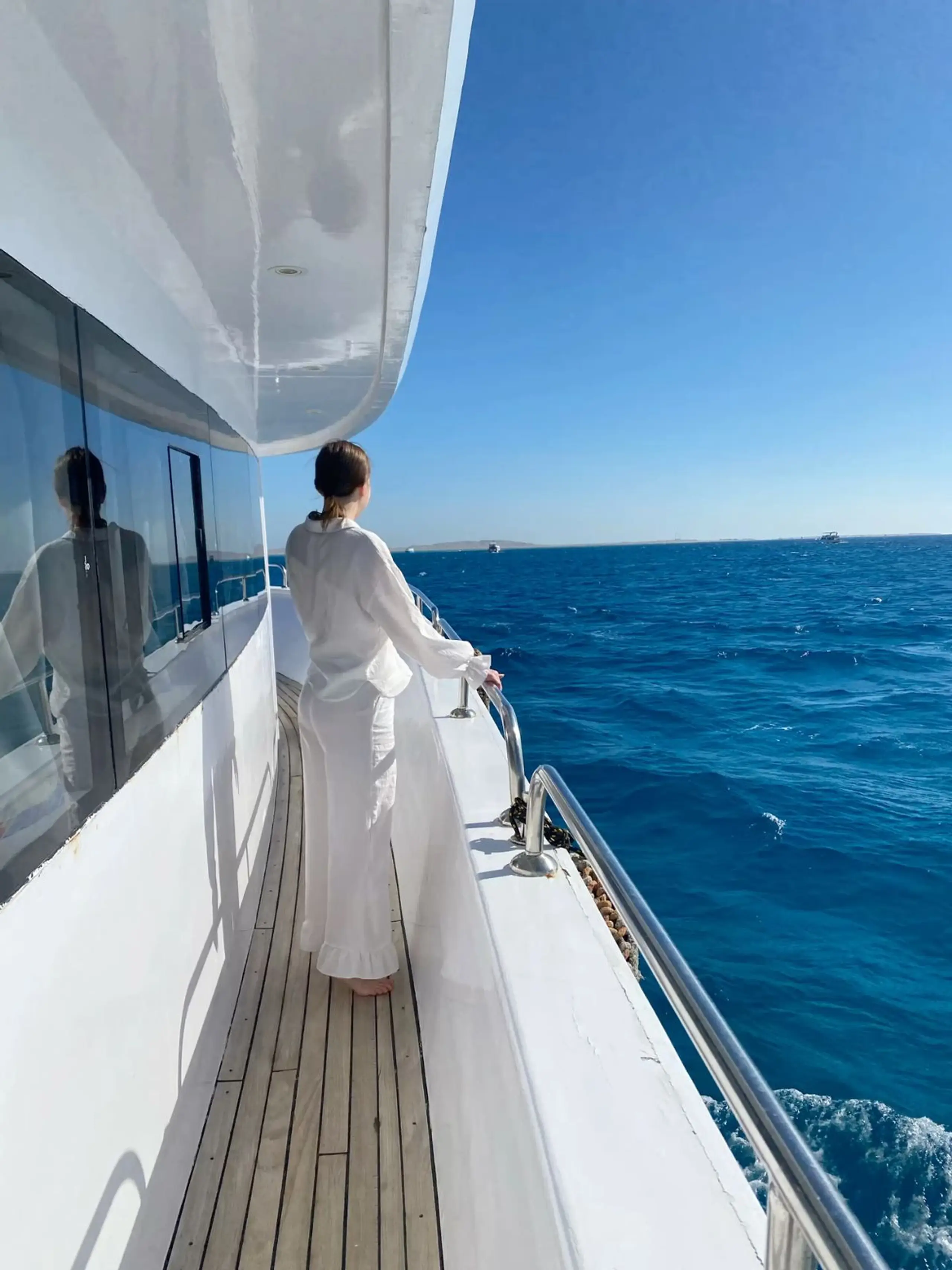 Woman in white standing on a yacht deck overlooking the open sea