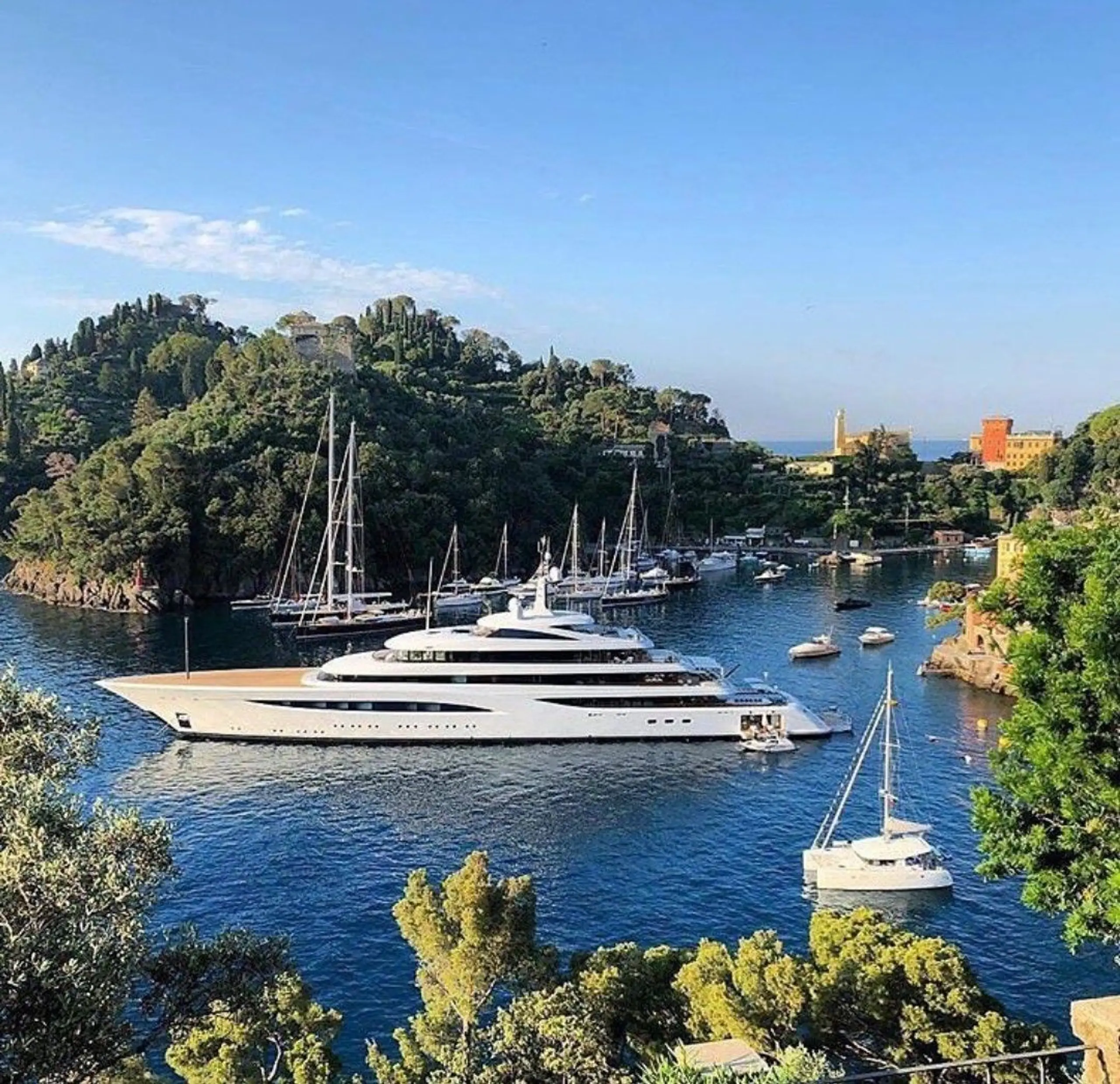 Superyacht anchored in a Mediterranean harbour surrounded by greenery.