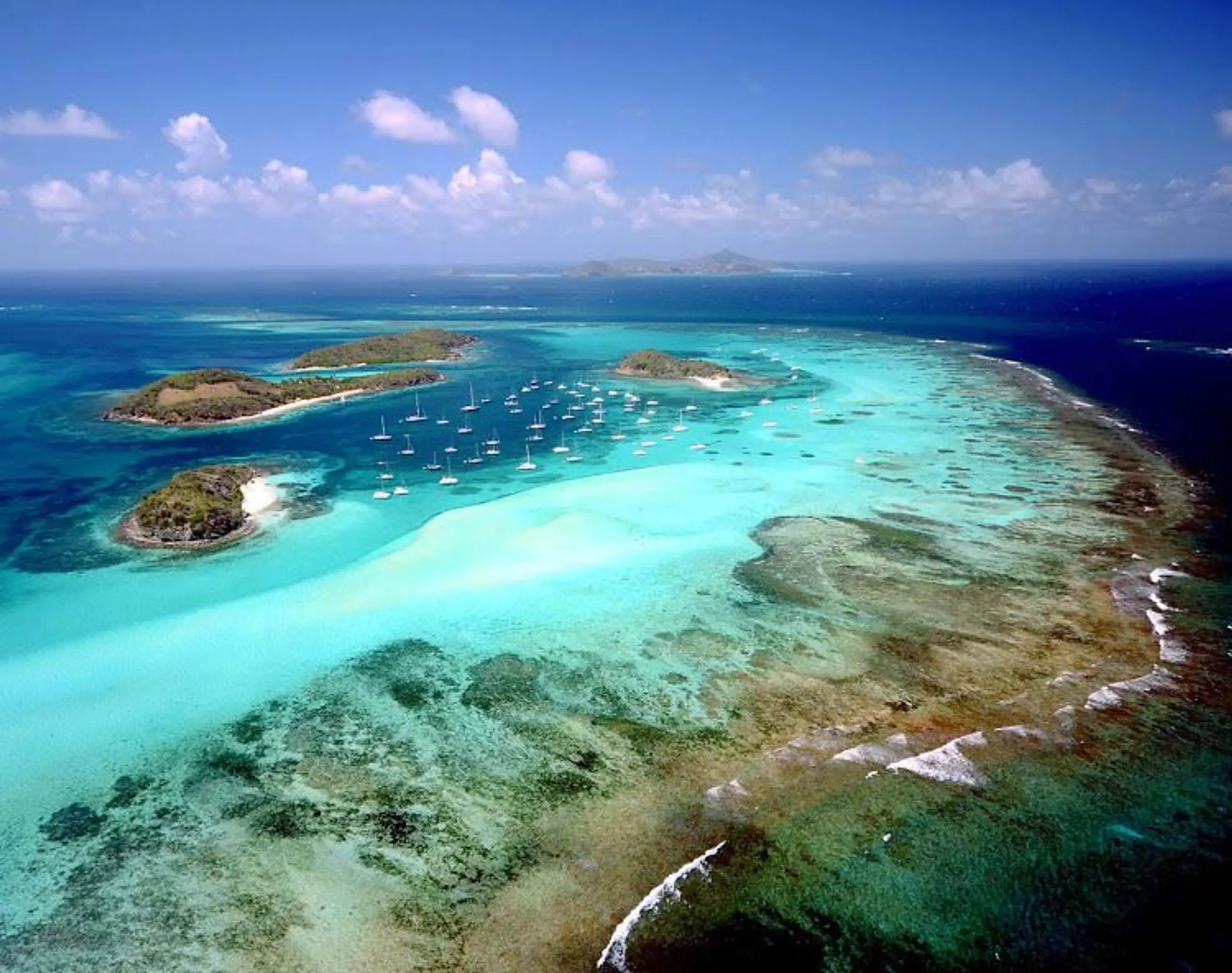 Aerial view of tropical islands and yachts anchored in clear turquoise water.