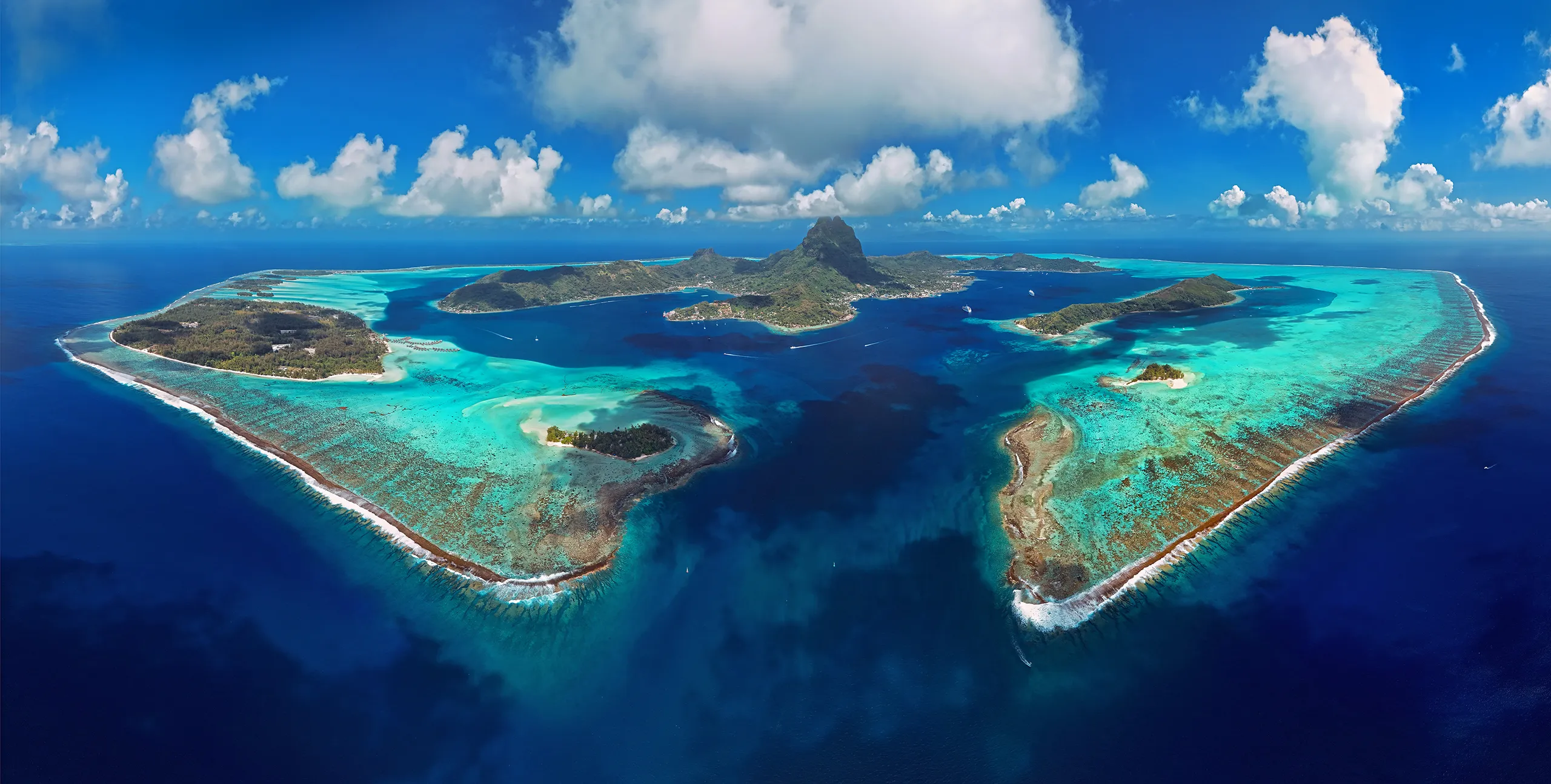 Aerial panoramic view of Bora Bora lagoon in French Polynesia with turquoise reefs, tropical islets, and Mount Otemanu in the center