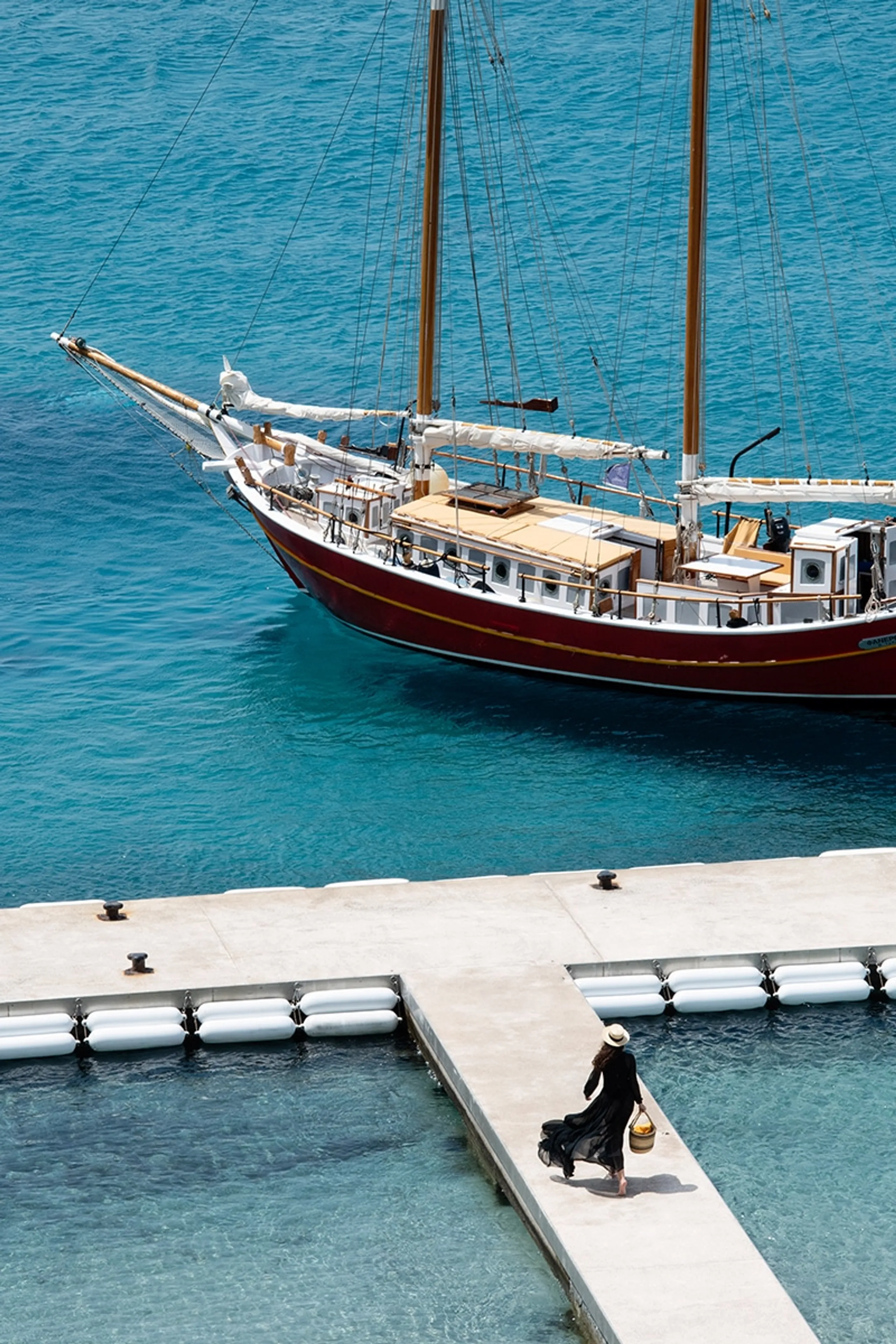 Classic sailing yacht moored beside a Mediterranean marina with a woman walking on the pier